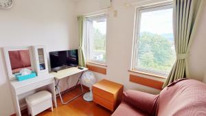 a living room with a desk and a tv and two windows at Pension and Restaurant La Collina in Nakafurano