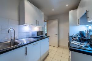 a kitchen with white cabinets and a sink and a microwave at Chelsea Pelham Apartments in London