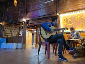 Ein Mann, der auf einem Stuhl sitzt und Gitarre spielt in der Unterkunft Son Thuy Homestay in Ha Giang