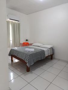 Cama en habitación blanca con silla roja en Hotel Monte Arau en Boa Vista