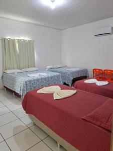 three beds in a room with red sheets at Hotel Monte Arau in Boa Vista