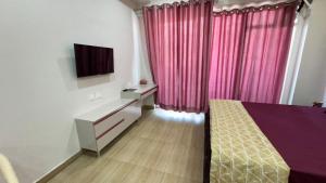 a bedroom with a bed and a tv and pink curtains at Namoh studio and apartment in Ghaziabad