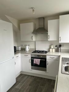 uma cozinha com armários brancos e um forno com placa de fogão em Village House Cardiff - Close to A48 and M4 em Cardiff