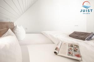 a white bedroom with a book on the bed at Landhaus Gertrude 105 - Wohnung Wattenmeer in Juist