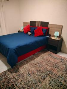 a bedroom with a blue bed with red pillows and a rug at Reutlwane Gardens Apartments in Secunda