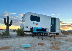 an rv parked in the desert with a table and chairs at Tarantula Ranch Campground & Vineyard near Death Valley National Park in Amargosa Valley