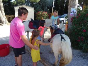 a man and two children petting a white pony at Camping Les Flamants Roses 4 in Saint-Nazaire
