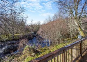 a wooden fence next to a river with trees at Wildside Highland Lodges in Whitebridge