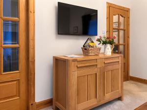 a room with a television on a wall with a wooden cabinet at Hilton Farm Steadings in Limekilns