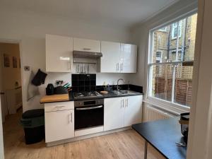 La cuisine est équipée de placards blancs et d'un four avec plaques de cuisson. dans l'établissement 2 Bedroom flat 10 min walk to tube, à Londres