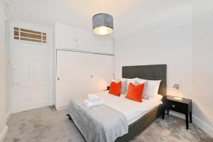 ein weißes Schlafzimmer mit einem Bett mit orangefarbenen Kissen in der Unterkunft London Choice Apartments - Baker Street- Regent's Park in London