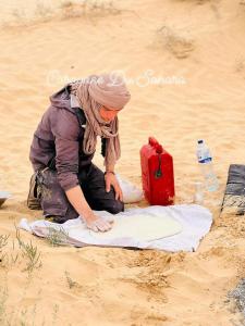 a woman kneeling in the sand with a red suitcase at Private Camp25km-from DOUZ in Douz