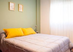 a bed with a yellow pillow and a window at Moreno home in La Plata