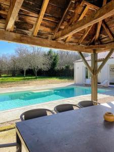 uma mesa e cadeiras sob um telhado com uma piscina em Maison de caractère au cœur de la Haute-Saintonge. em Champagnolles