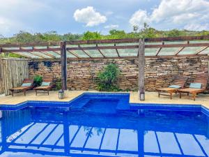 a swimming pool with chairs and a stone wall at Pousada Sete Quedas in Carrancas