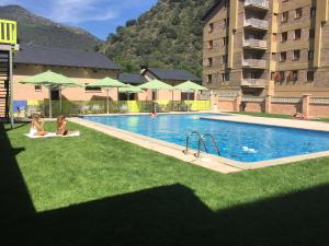 zwei Personen sitzen auf dem Gras in der Nähe eines Swimmingpools in der Unterkunft Hotel Victor in Rialp