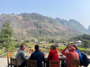 Du Gia Cozy Homestay & Tours في Làng Cac: مجموعة من الناس يجلسون على طاولة مع جبال في الخلفية