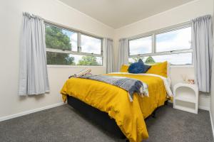 a bedroom with a yellow bed and windows at Riverside Retreat in Whangarei