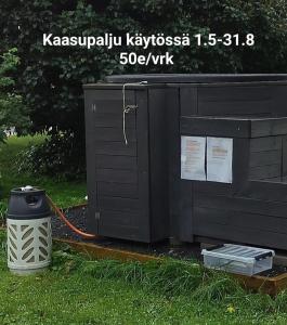 Una casa negra con un cubo de basura al lado. en Koskela en Kalajoki