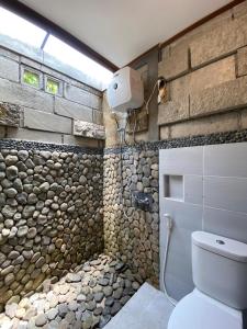 baño con pared de piedra y aseo en Djiwanta Cottage by Balkondes Sambirejo, en Groyokan