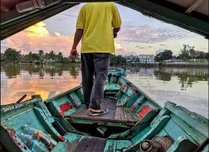 Ein Mann steht auf einem Boot im Wasser in der Unterkunft [Netflix] Holiday Getaways Suite@ Riverine Kuching in Kuching