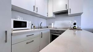 eine weiße Küche mit weißen Schränken und einer Mikrowelle in der Unterkunft Zuhayra Beach Apartamento con Vista a 50m del Mar in Torrox Costa