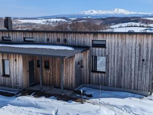 ein Holzgebäude im Schnee mit Schnee in der Unterkunft Meiji no Okano Yado in Biei