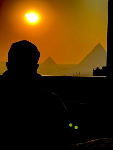 a silhouette of a man looking at the pyramids at sunset at pyramids old stone view in Cairo