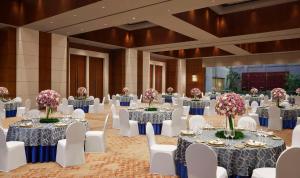 um salão de baile com mesas redondas, cadeiras brancas e flores em Hyatt Regency Kolkata em Calcutá