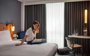 Eine Frau, die auf einem Bett sitzt und ein Buch liest. in der Unterkunft Hyatt Regency London Stratford in London