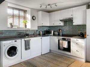 a kitchen with white cabinets and a washer and dryer at Birdsong Cottage in Hartland