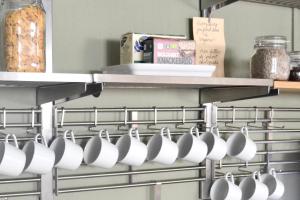 un montón de tazas blancas colgando de un estante en una cocina en HEMMET Simrishamns vandrarhem och B&B, en Simrishamn