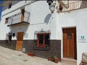 - un bâtiment blanc avec des portes en bois et un balcon dans l'établissement Casa De Juanita Vivienda Rural, à Hinojares