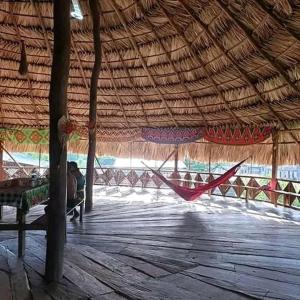 a person sitting on a bench under a straw roof at Hospedaje Agroturismo Wounaan in Pidiaque