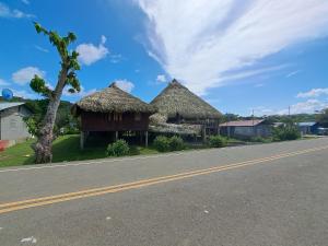 dwie chatki pokryte strzechą na poboczu drogi w obiekcie Hospedaje Agroturismo Wounaan w mieście Pidiaque