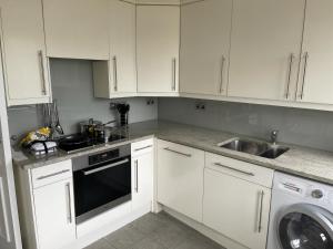 cocina con armarios blancos, fregadero y lavavajillas en Upper Berkely By Falcon Group en Londres