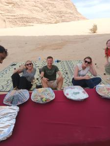 eine Gruppe von Menschen, die um einen Tisch mit Teller Essen sitzen in der Unterkunft Sunrise Luxury Camp in Wadi Rum