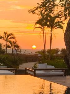 um pôr-do-sol sobre uma praia com palmeiras e uma piscina em Villa Praia - La Villa Group em Jericoacoara