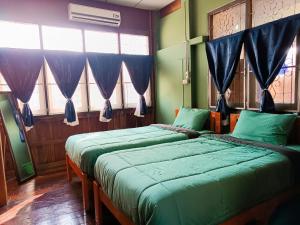 two beds in a room with windows and blue curtains at PAI BAAN Homestay ปายบ้าน โฮมสเตย์ ถนนคนเดินปาย in Pai