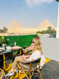 Capital Of Pyramids Hotel في القاهرة: امرأة جالسة على كرسي وتطل على الاهرامات