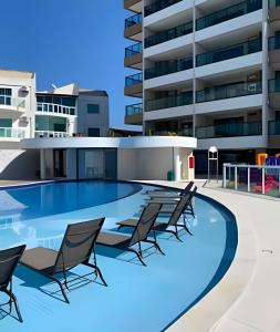 een zwembad met stoelen en een gebouw bij Apartamentos de 2 quartos com piscina na Praia dos Anjos in Arraial do Cabo