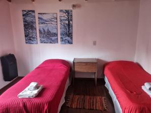 2 Betten in einem kleinen Zimmer mit roter Bettwäsche in der Unterkunft Casa Rural Bella Zaira in El Calafate