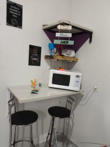 a table with a microwave and two bar stools at Kitnet Aconchegante in Foz do Iguaçu