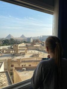 een vrouw die uit een raam naar een stad kijkt bij TOUT KING PYRIMDS VIEW in Caïro