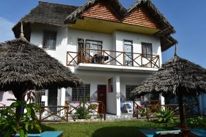 a white house with a balcony and two straw umbrellas at Pineapple House in Nungwi