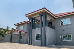 une grande maison avec des colonnes bleues dans une allée. dans l'établissement Cony’s Guest House, à Kwabenyan