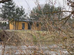 a yellow house behind some trees and a river at Domek całoroczny nad rzeką Wkra in Pomiechówek