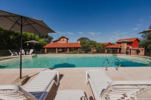 a swimming pool with white chairs and an umbrella at Cerro de los Duendes in Santa Rosa de Calamuchita