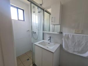 La salle de bains blanche est pourvue d'un lavabo et d'une douche. dans l'établissement New Door Apartments, à Nadi