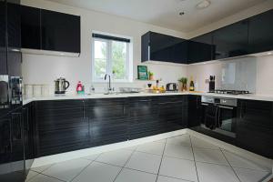 a kitchen with black cabinets and white tile floors at Luxury Apartment with Balcony, Fast WIFI, Smart TVs and Free Parking by Yoko Property in Milton Keynes